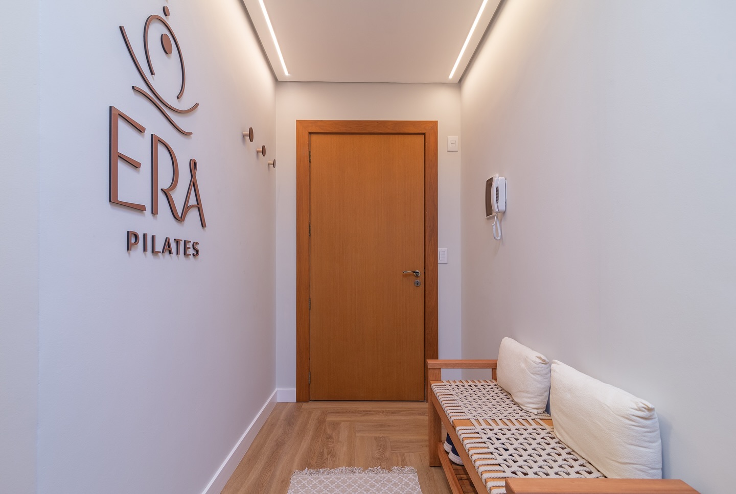 Hall de entrada com banco de palha e a marca ERA Pilates