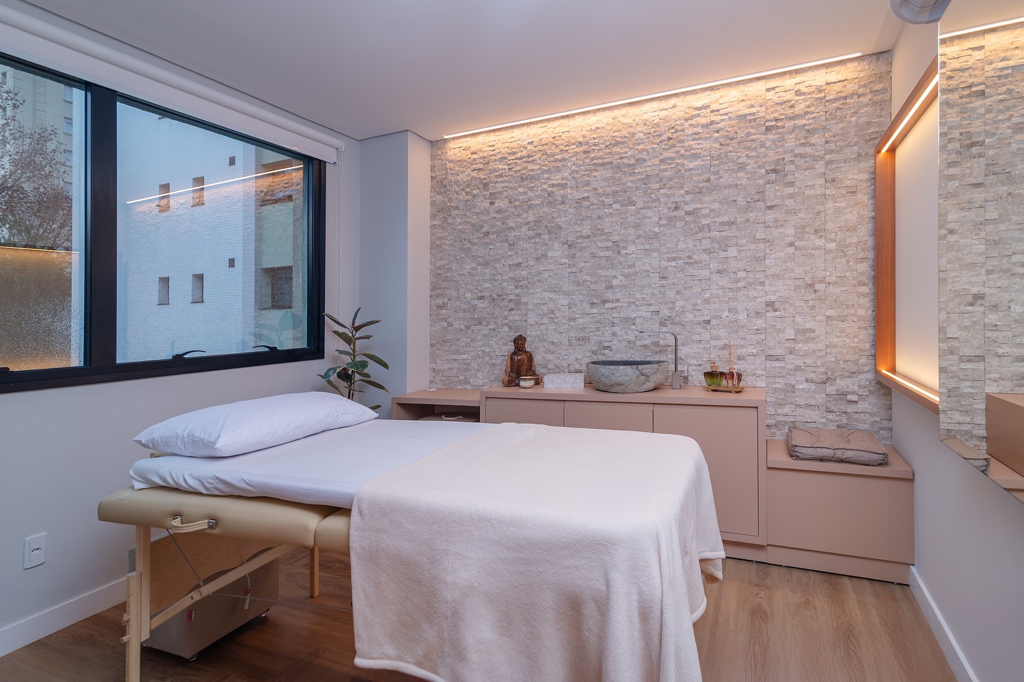 Sala de massagem com parede de pedra natural, maca e Buda
